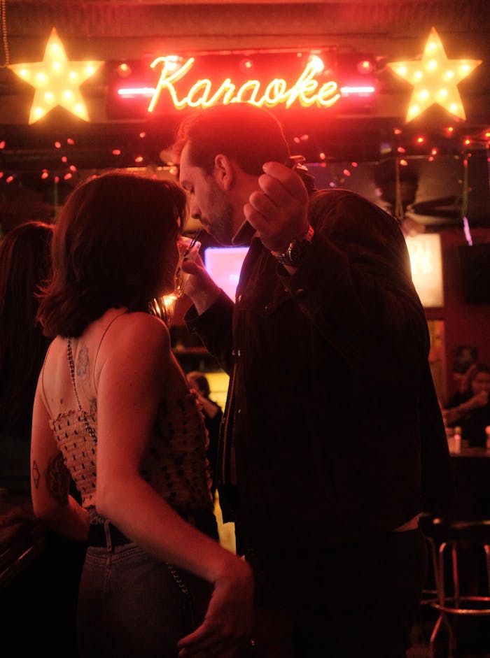 about-us A couple enjoying a lively karaoke night in a dimly lit bar setting with neon lights.